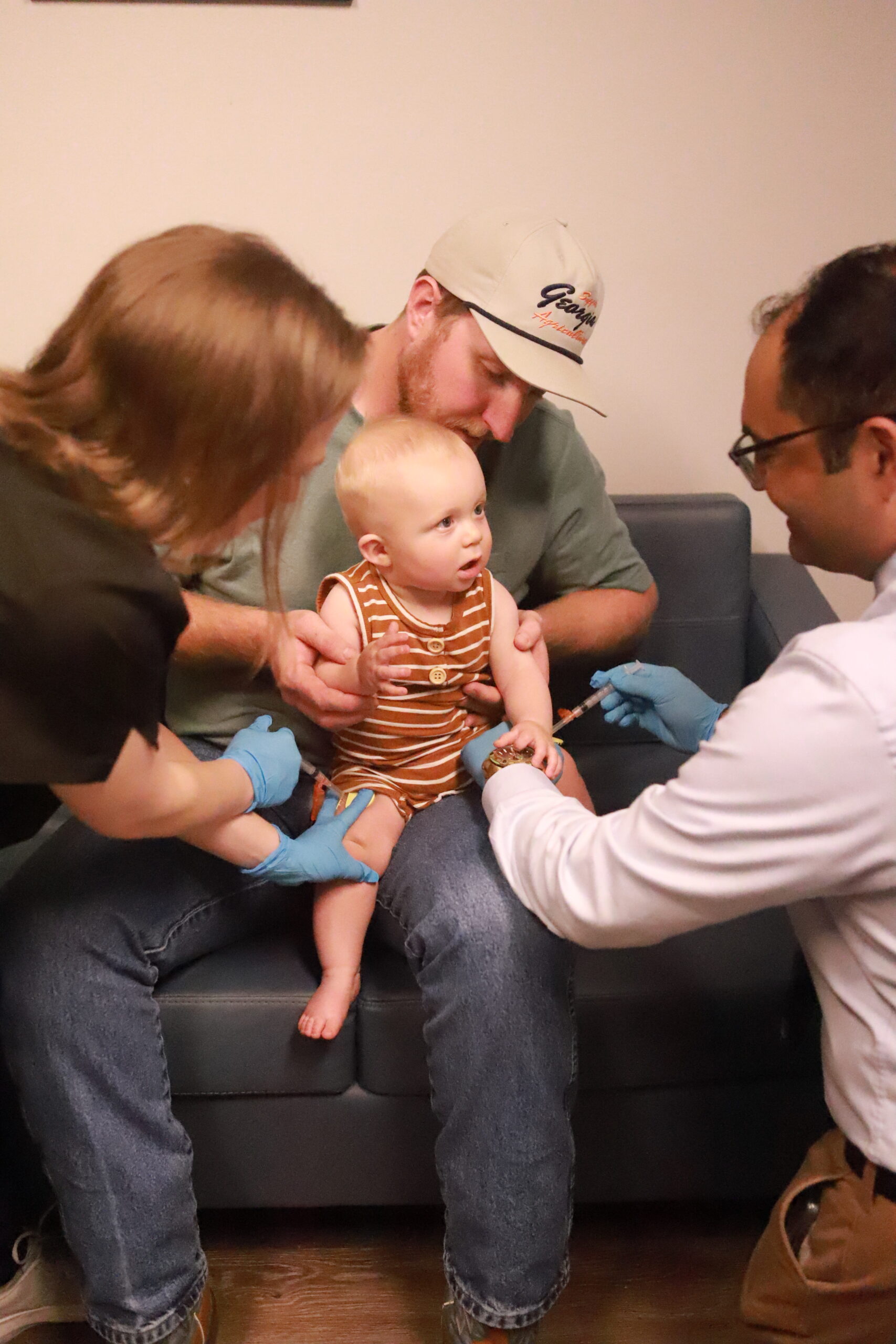 PIcture of a child, sitting on his father's lap, receiving a vaccine at Canopy Pediatrics with Dr. Homann and his nurse.